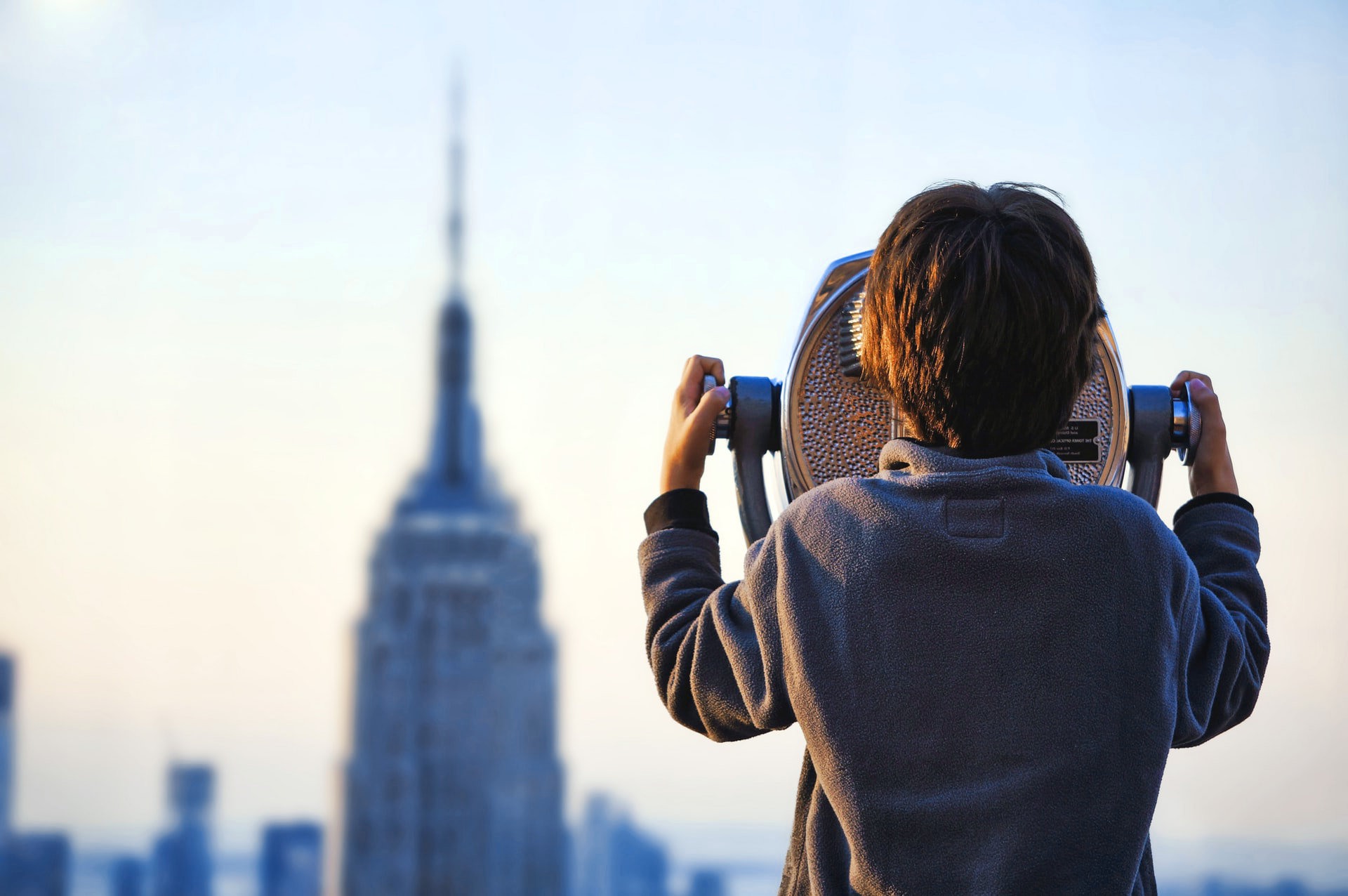 Junge schaut mit Fernglas auf ein Hochhaus.